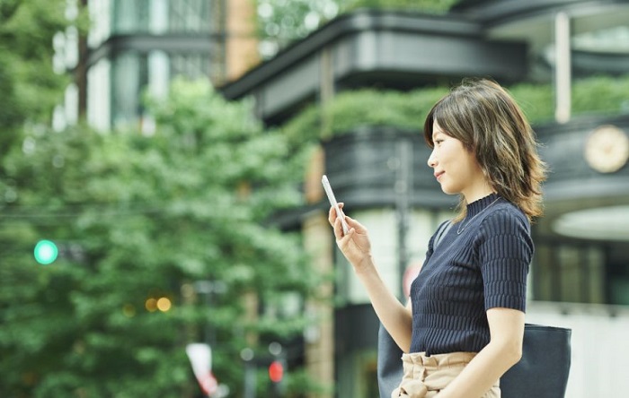 街中でスマホに目をやる女性社会人